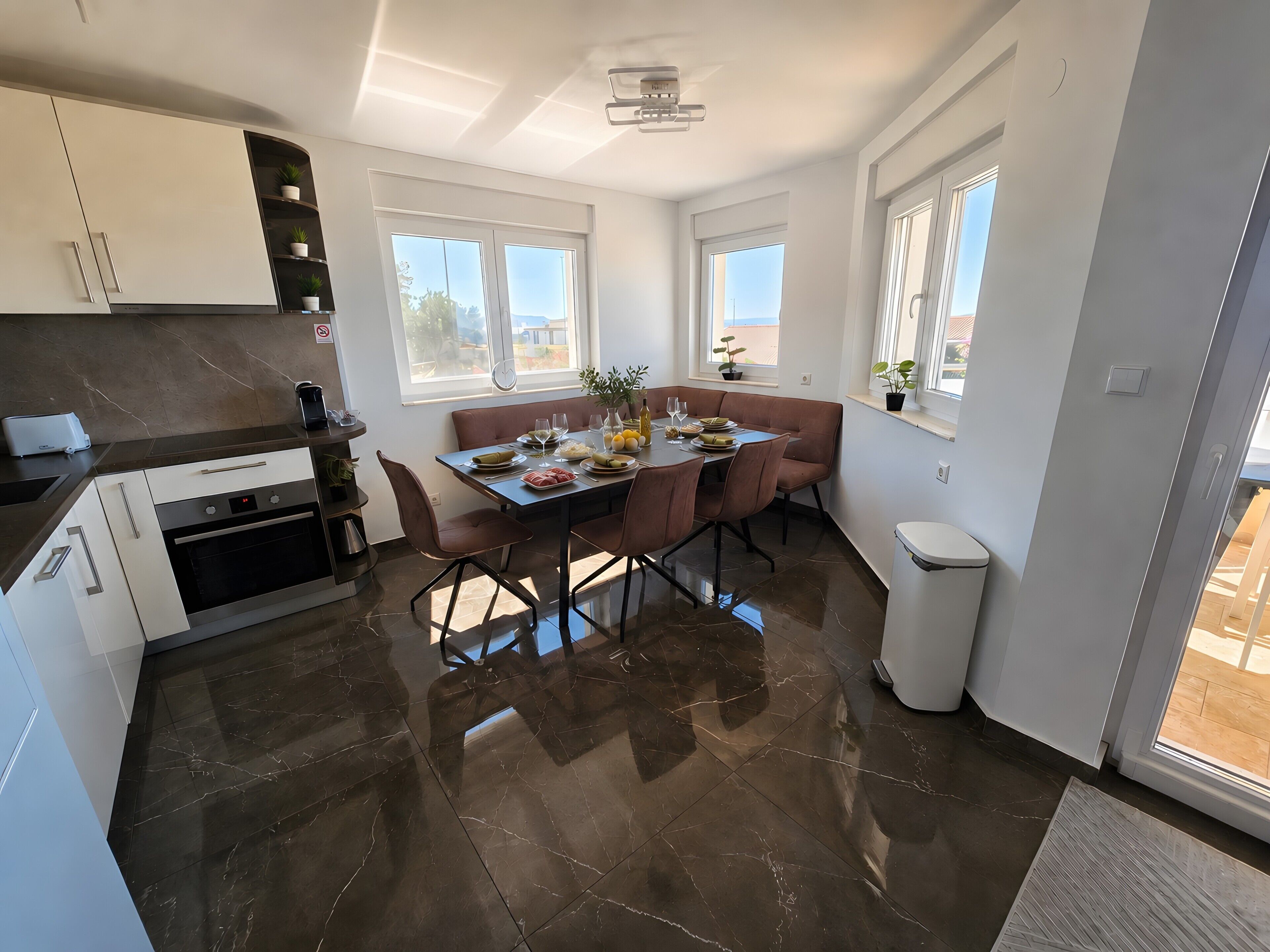 Una cocina moderna con zona de comedor, ventanas amplias y piso cubierto de baldosas.