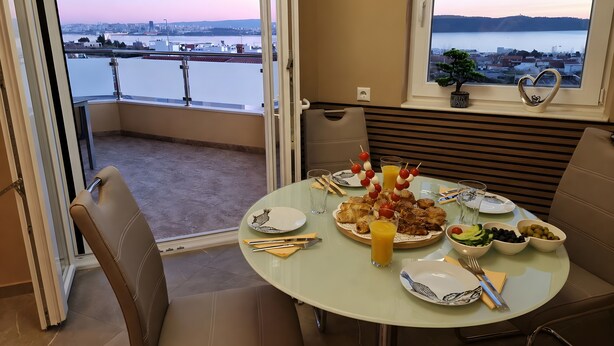 A dining area with a table set for two, overlooking a cityscape and water. - Villa 'Rocco-Salzwasserpool-Split' with Wi-Fi (Kaštel Gomilica)