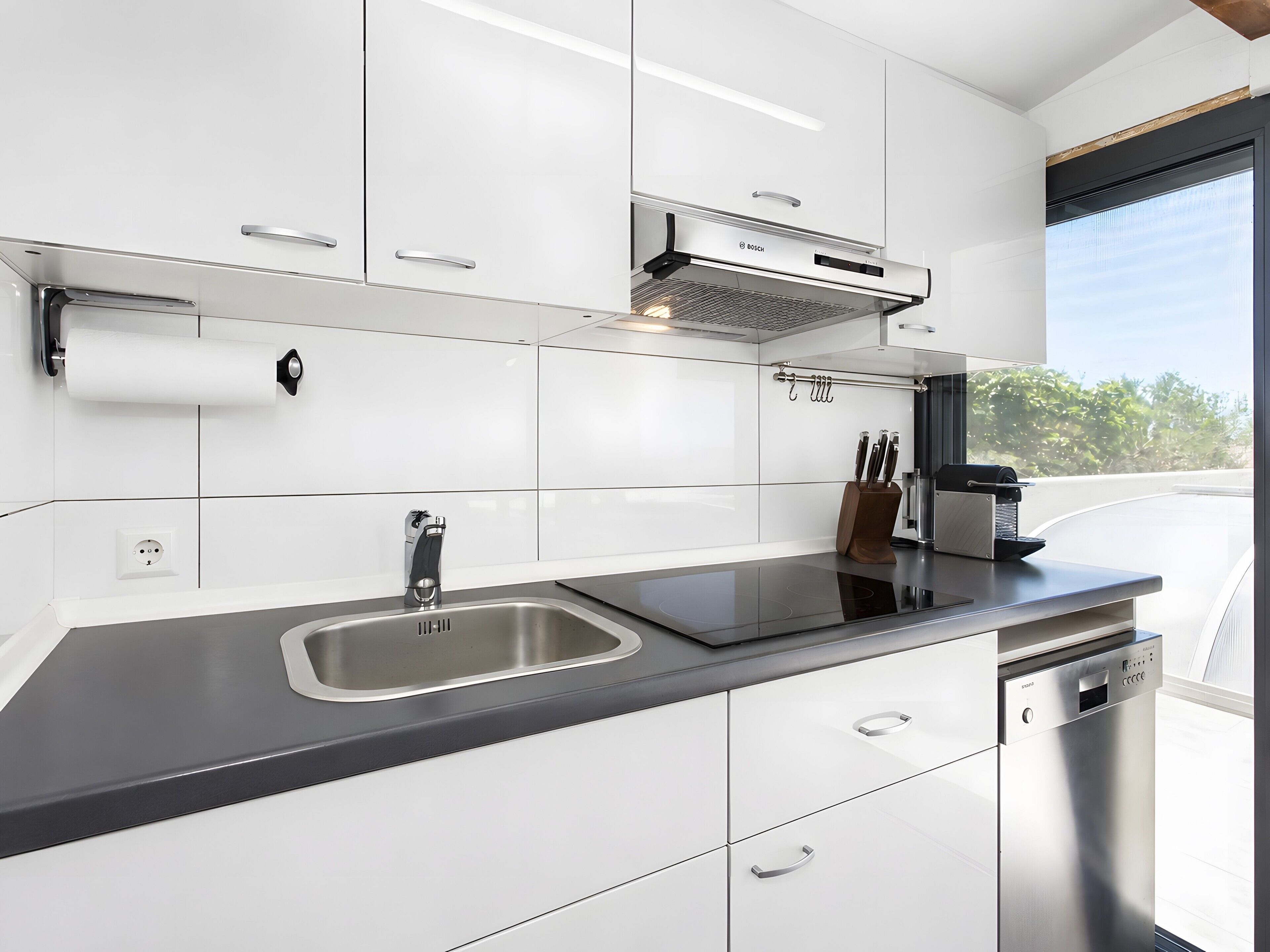 Una cocina moderna con armarios blancos, un lavamanos de acero inoxidable y un lavavajillas Bosch.