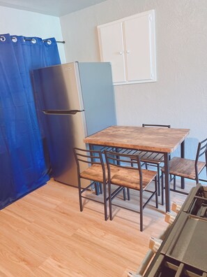 A compact kitchen with a refrigerator, a wooden dining table with chairs, and a blue curtain. - Pet friendly/Fully fenced/3 bedroom house/King beds (Oklahoma City)