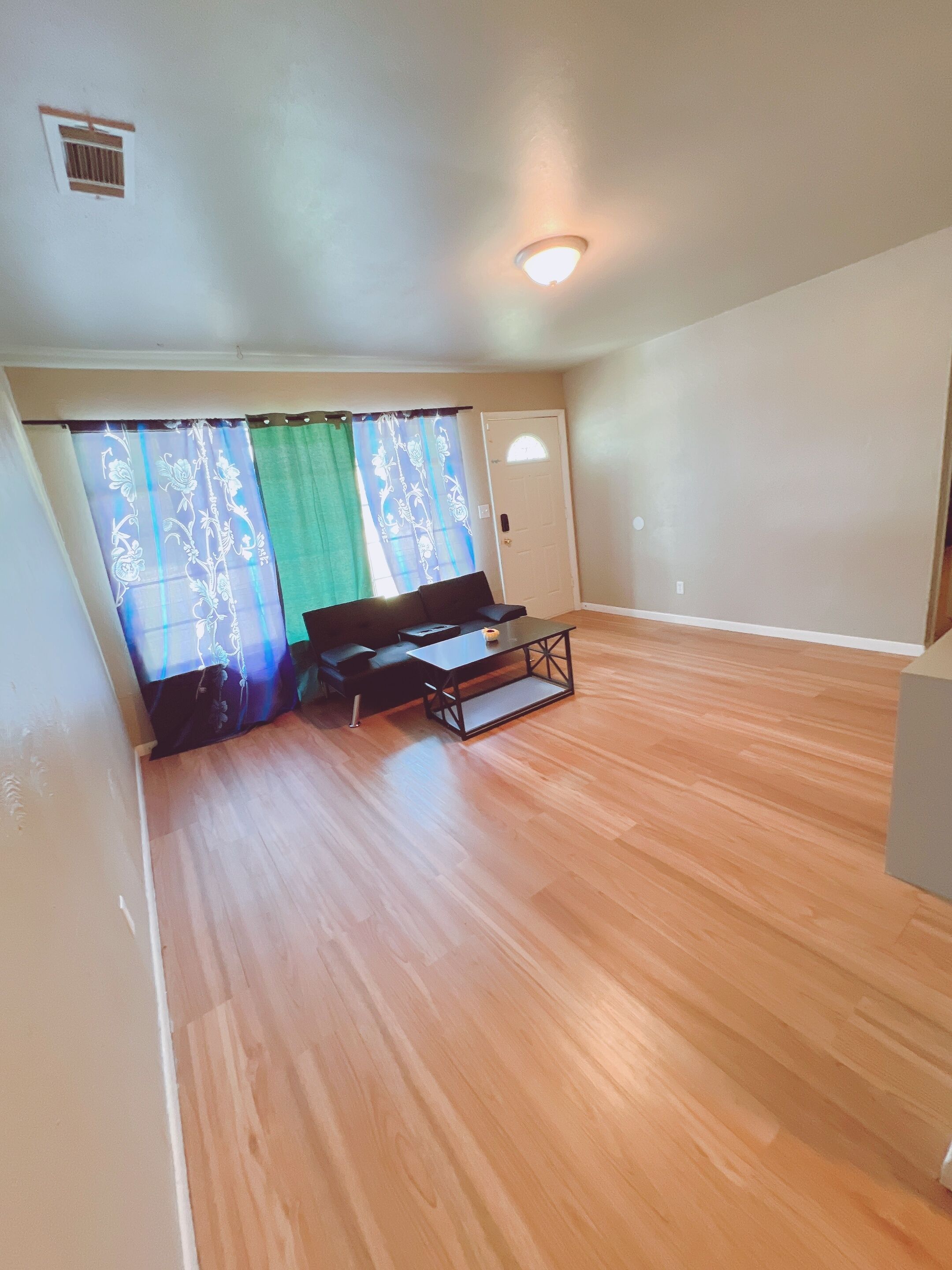 A room with a wooden floor, a sofa, a coffee table, and a window with curtains.