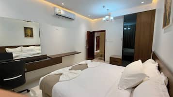 A hotel room with a bed, bedside table, mirror, air conditioning unit, and a door leading to a bathroom.