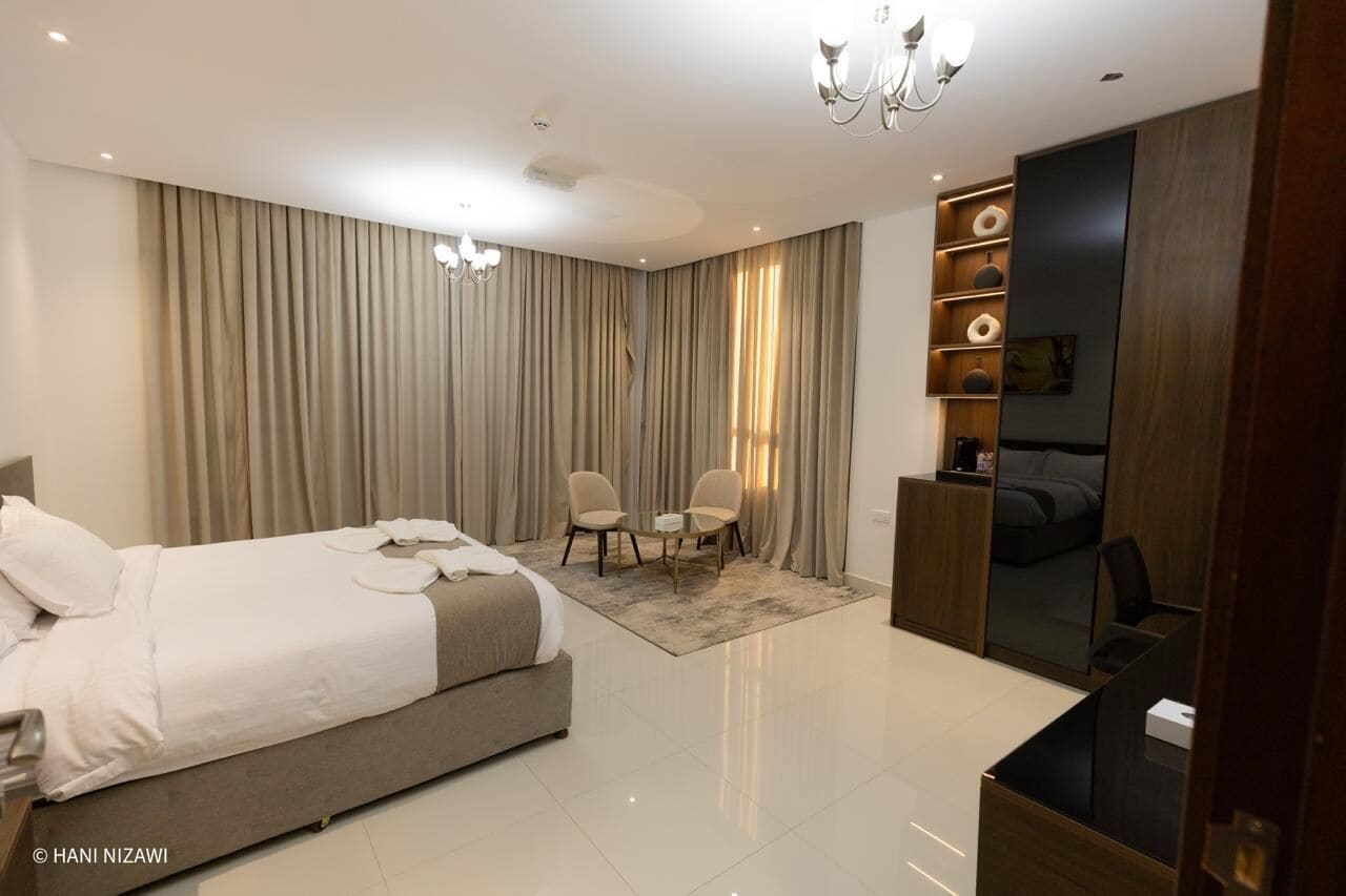 Une chambre moderne avec un grand lit, deux fauteuils, un bureau et un téléviseur.