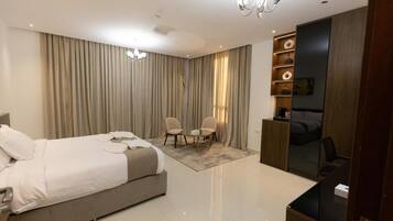 Une chambre moderne avec un grand lit, deux fauteuils, un bureau et un téléviseur.