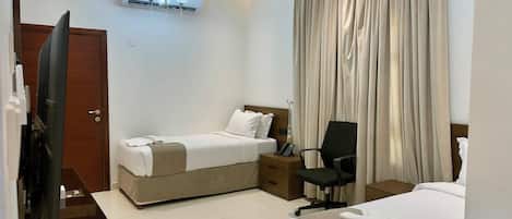 A hotel room with a bed, a desk, a chair, a TV, and a window with curtains.