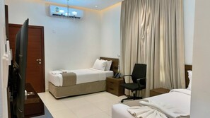 Une chambre d’hôtel avec un lit, un bureau, une chaise, une télévision et une fenêtre avec des rideaux.