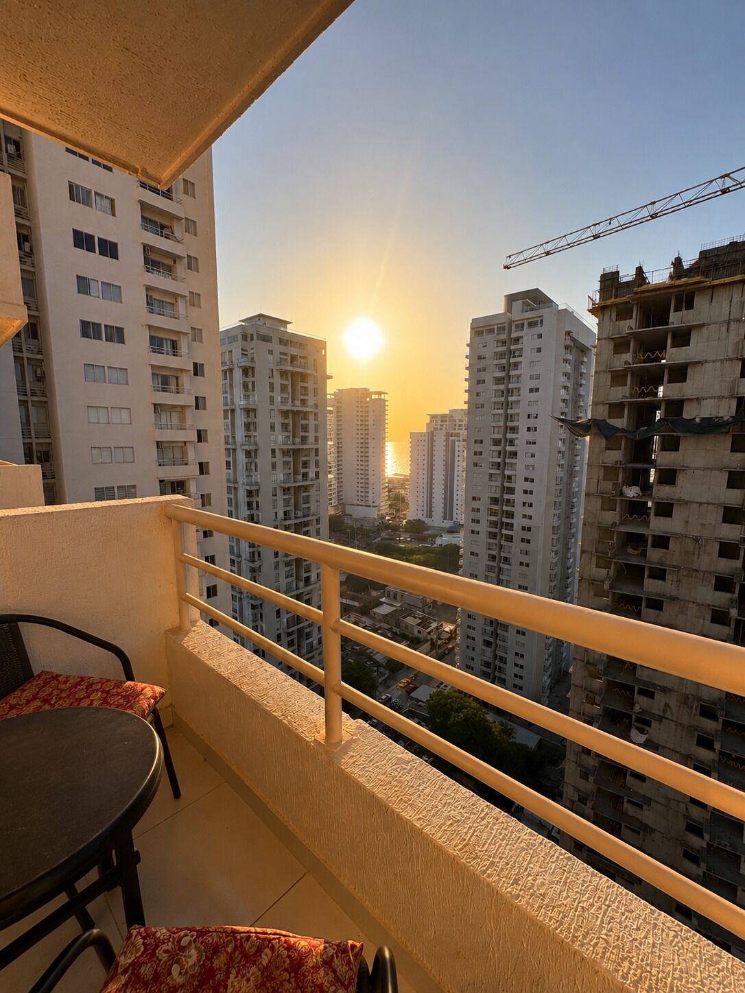 A balcony with a view of high-rise buildings and the sun setting in the background.
