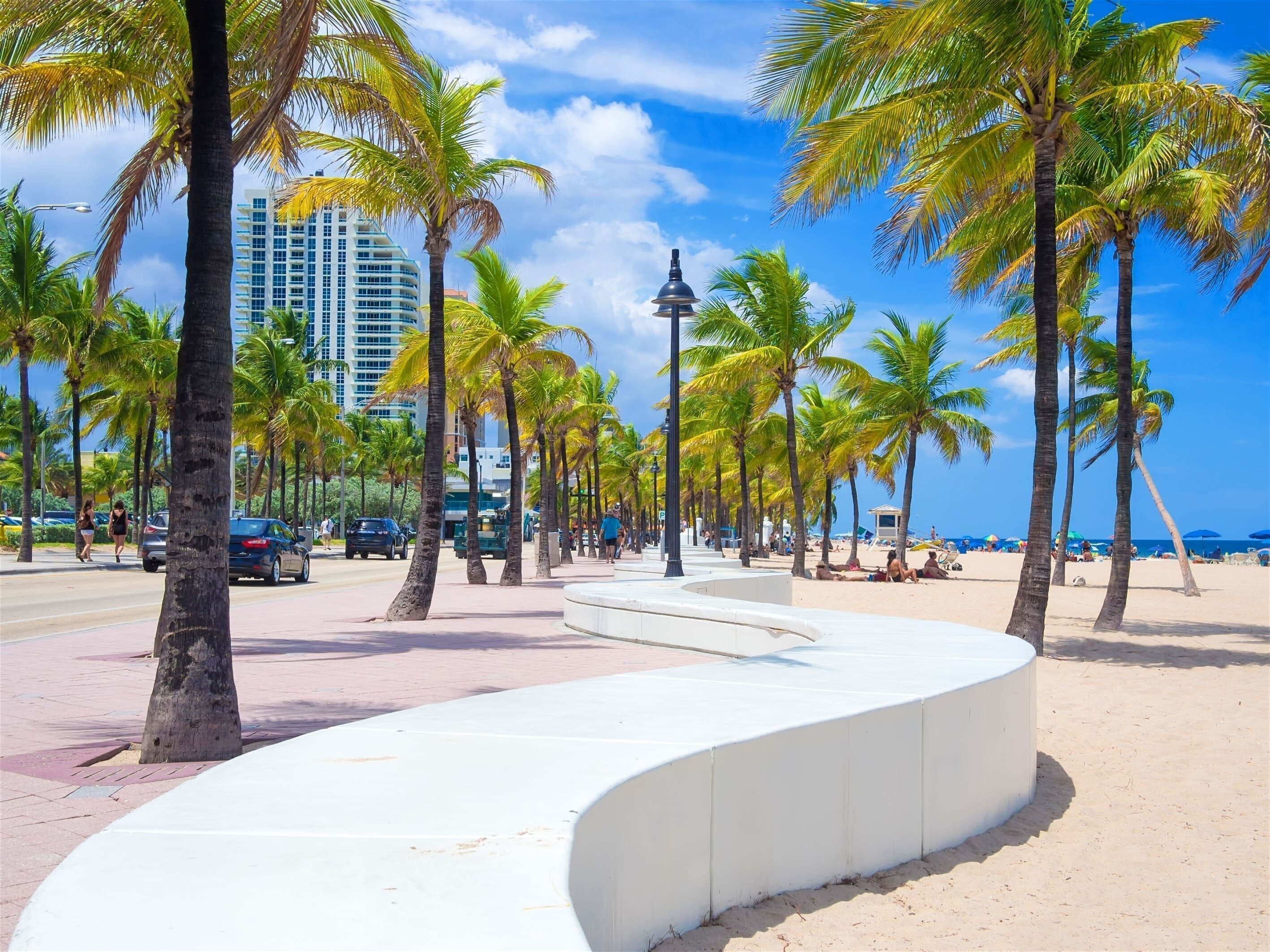 A curved white structure on a beach with palm trees and a clear sky.