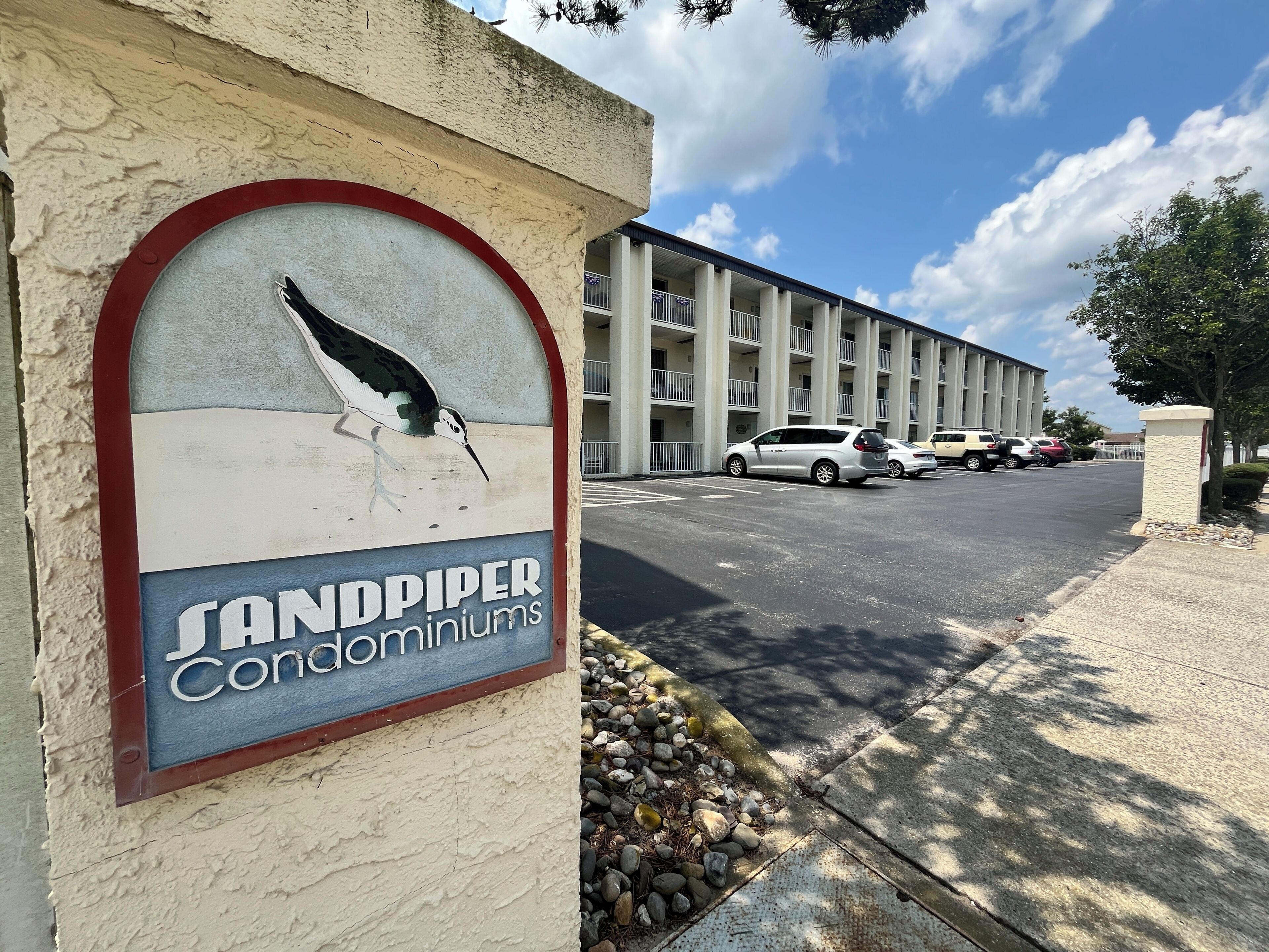 Une enseigne pour le complexe de copropriétés Sandpiper, avec une illustration d’un oiseau, un parking et un immeuble doté de balcons.