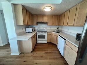 A compact kitchen with wooden cabinets, a white countertop, a built-in oven, a microwave, and a refrigerator. - Fantastic Ocean Front Condo Panoramic Skyline View Short Walk to Beach (Brigantine)