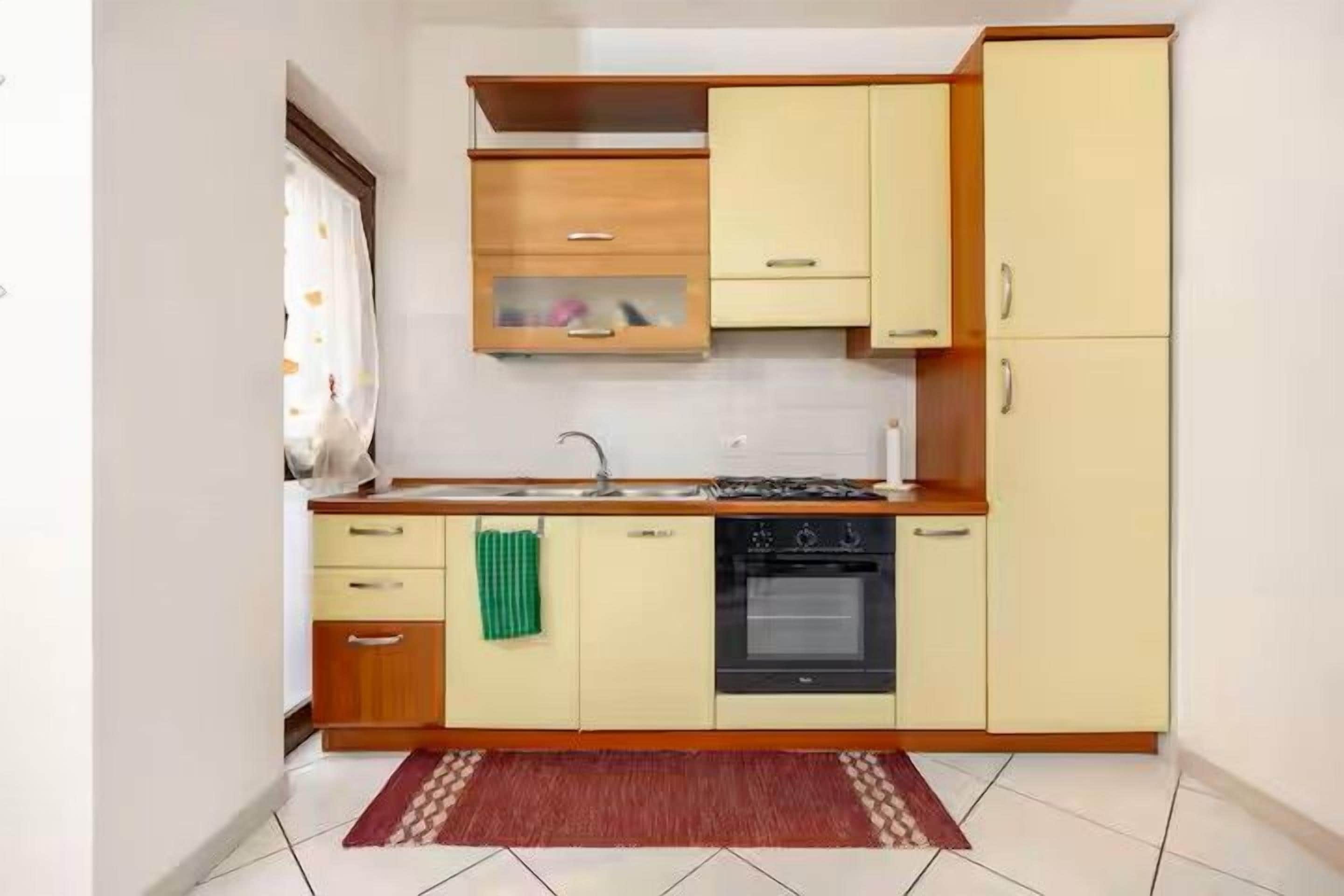 Cocina compacta con estufa, horno y lavamanos, armarios de madera y piso de baldosas.