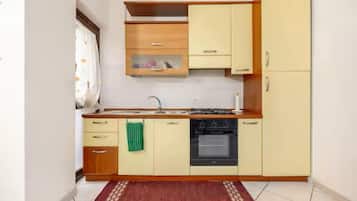 Cocina compacta con estufa, horno y lavamanos, armarios de madera y piso de baldosas.