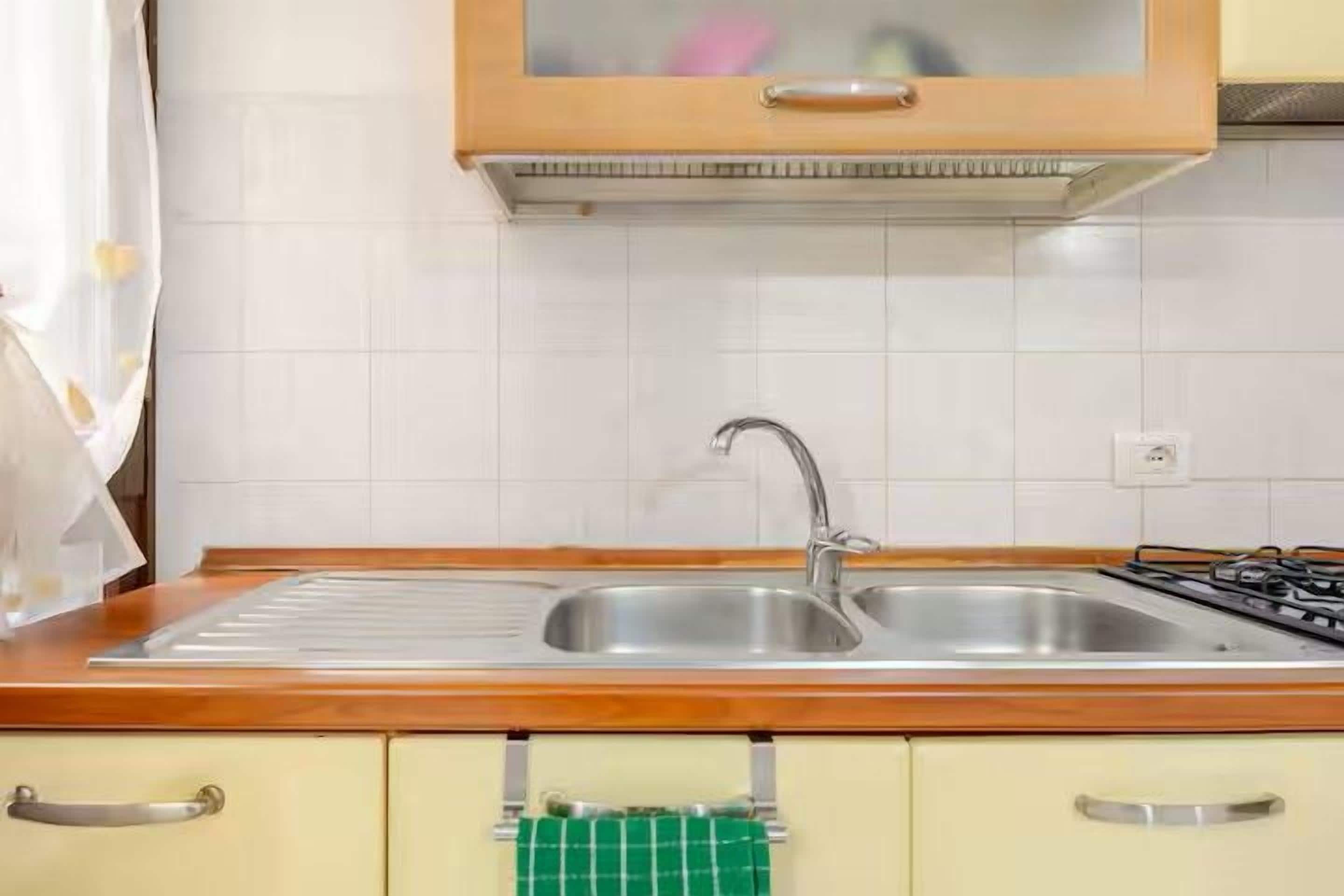 A kitchen with a stainless steel sink, wooden countertop, and a green towel hanging on a cabinet handle.