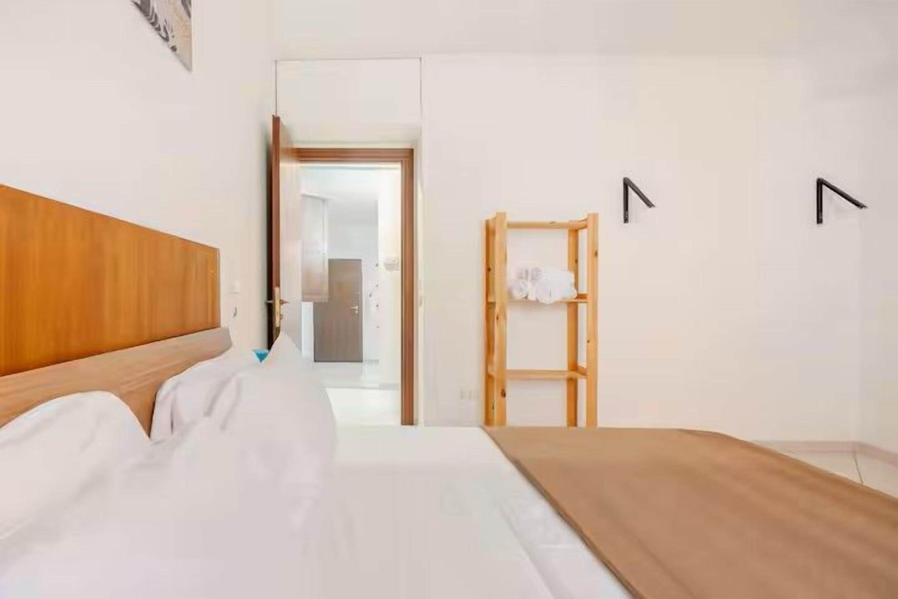 Una habitación de hotel con cabecera de madera, cama con ropa blanca, una banca de madera y un armario con espejo.