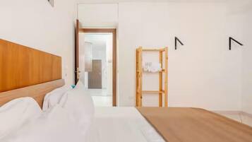 Una habitación de hotel con cabecera de madera, cama con ropa blanca, una banca de madera y un armario con espejo.