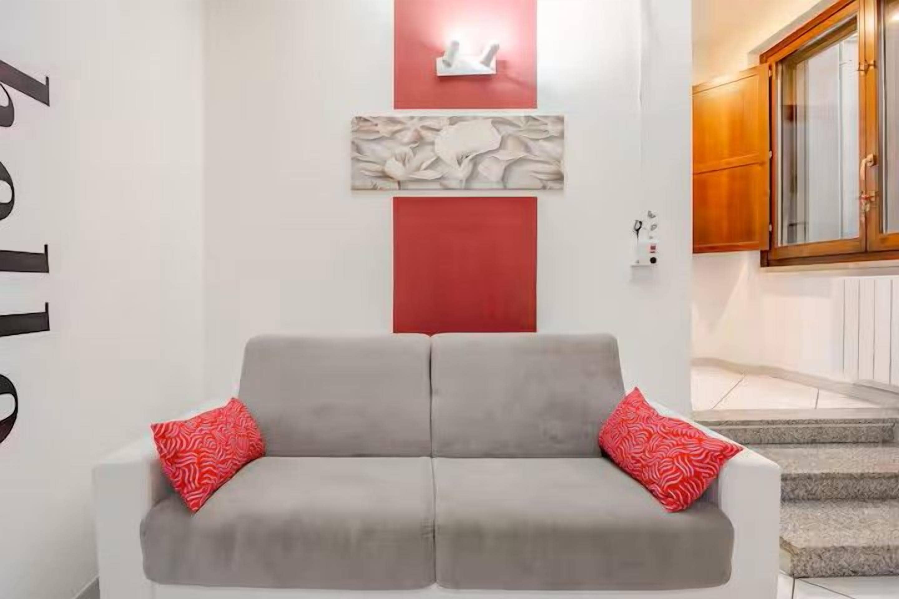 Un divano grigio con cuscini rossi in una stanza con una parete di accentuazione rossa e un armadio in legno.
