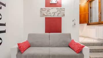Un divano grigio con cuscini rossi in una stanza con una parete di accentuazione rossa e un armadio in legno.