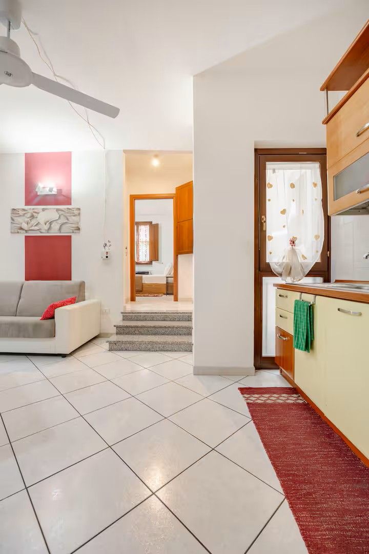 A modern living room with a sofa, a staircase leading to a bedroom, and a kitchen area.