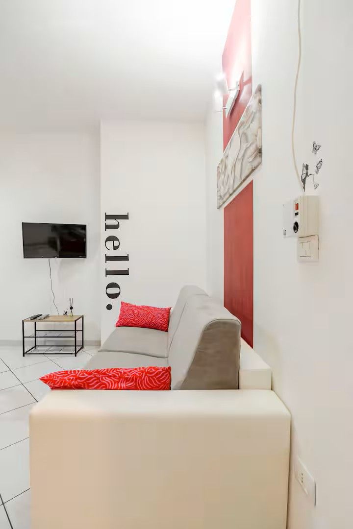 A modern living room with a sofa, a flat-screen TV mounted on the wall, and a small side table.