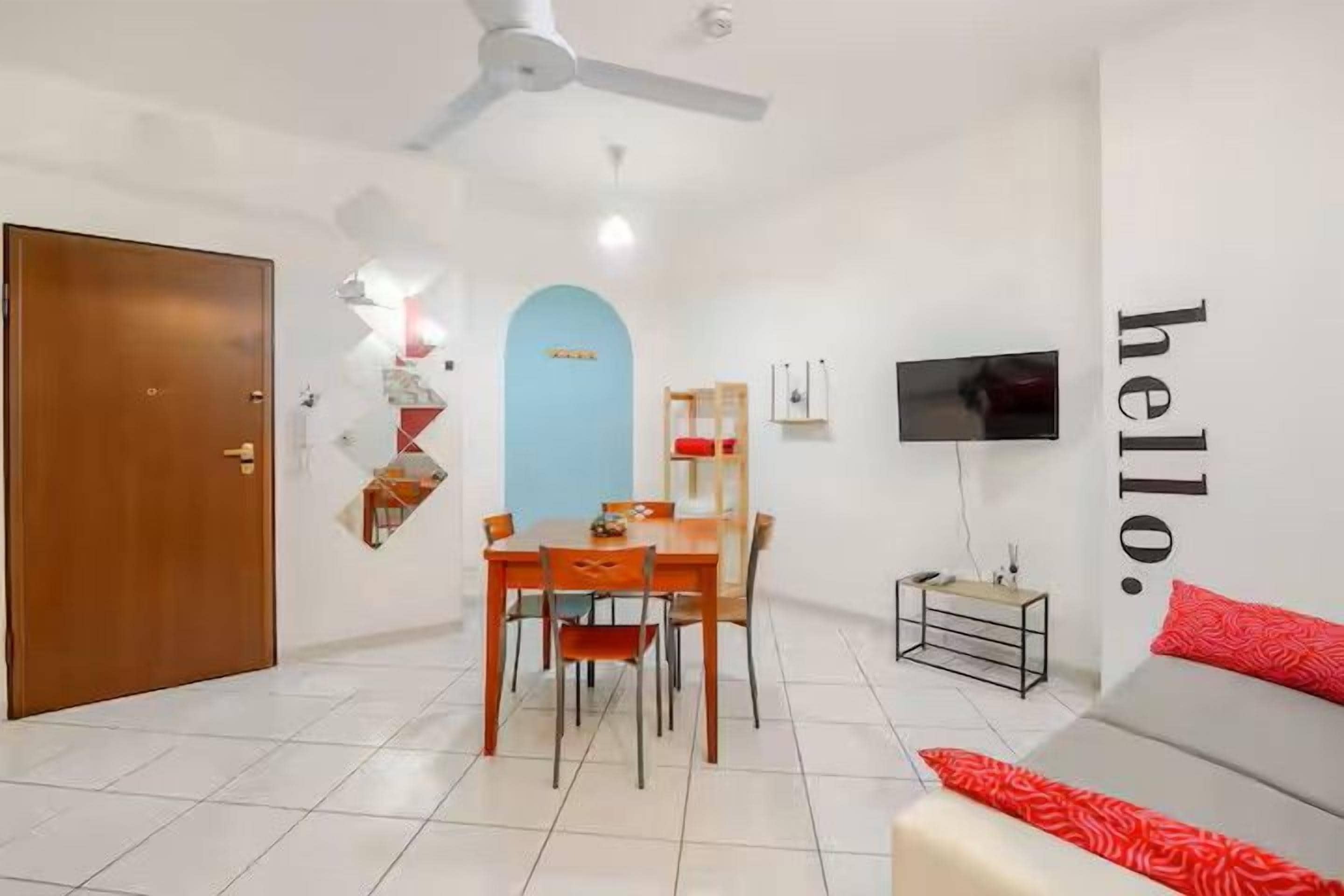 A modern living room with a dining area, a television mounted on the wall, and a door leading to another room.