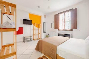 Quarto com uma cama beliche, uma cama de solteiro, televisão, janela com cortinas e radiador.