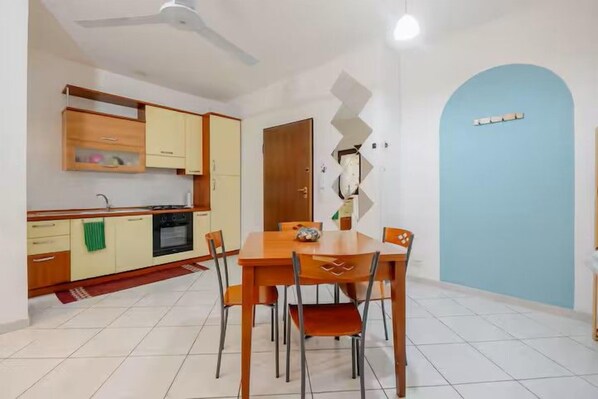 A dining area with a wooden table and chairs, a kitchen with wooden cabinets, and a blue door.