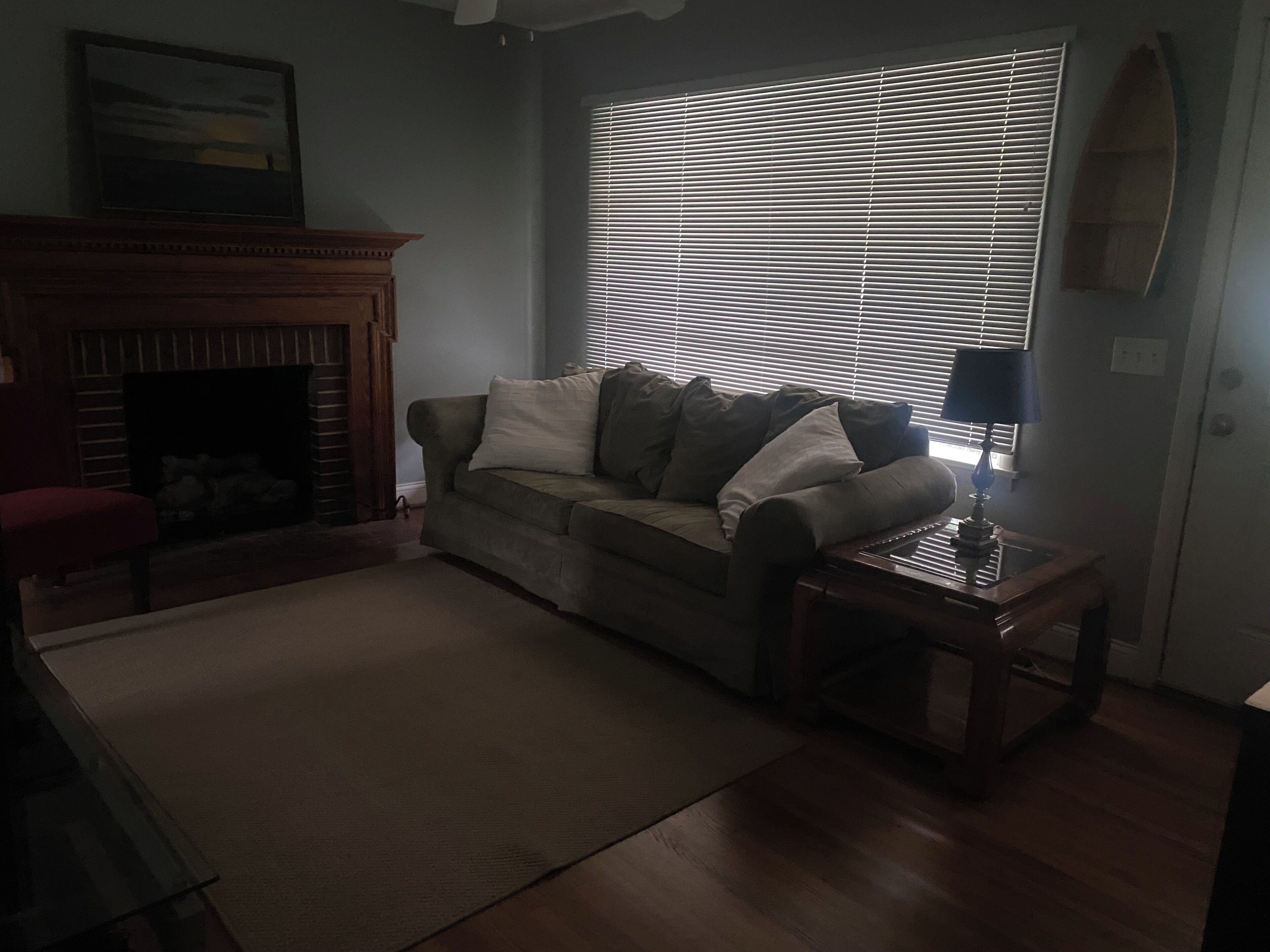 A living room with a sofa, a fireplace, and a window with blinds.
