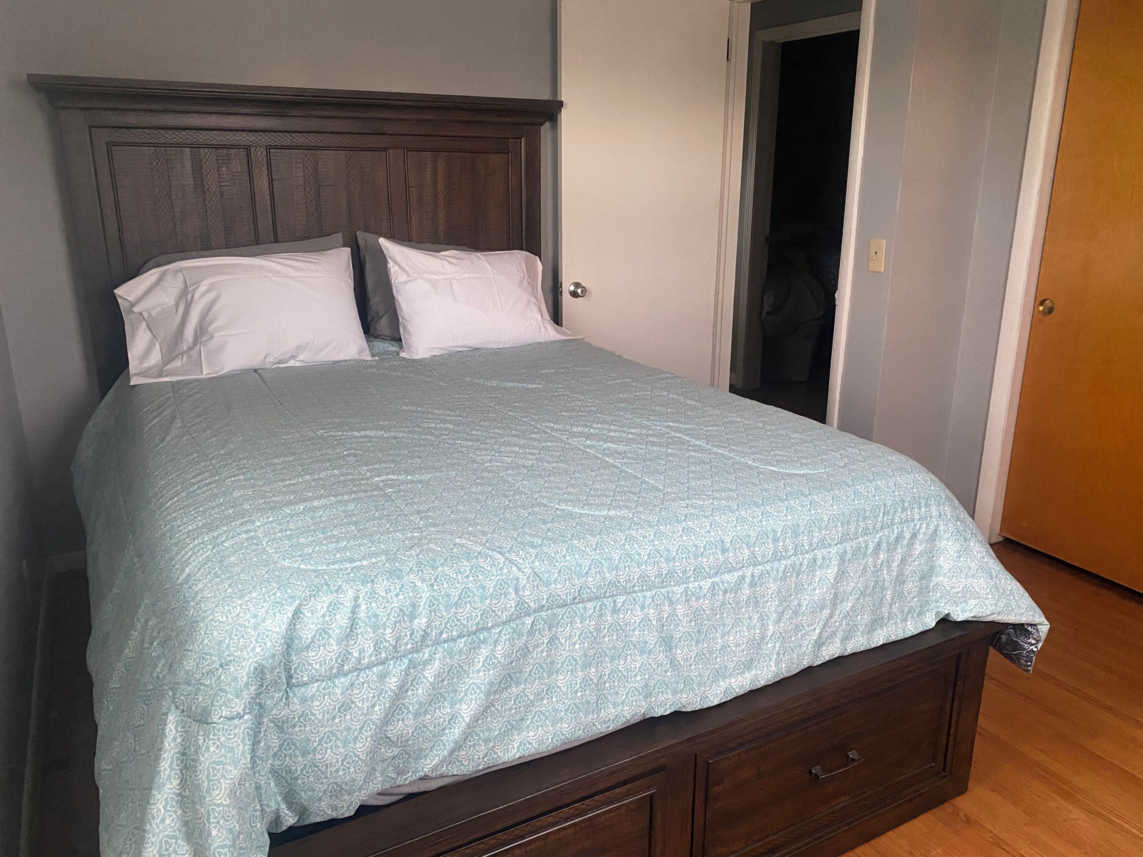 A single bed with a wooden headboard, a light blue patterned bedspread, and two white pillows.