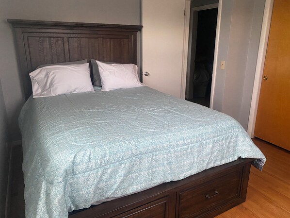 Ein Einzelbett mit Holz-Kopfteil, einer hellblauen, gemusterten Bettdecke und zwei weißen Kissen.