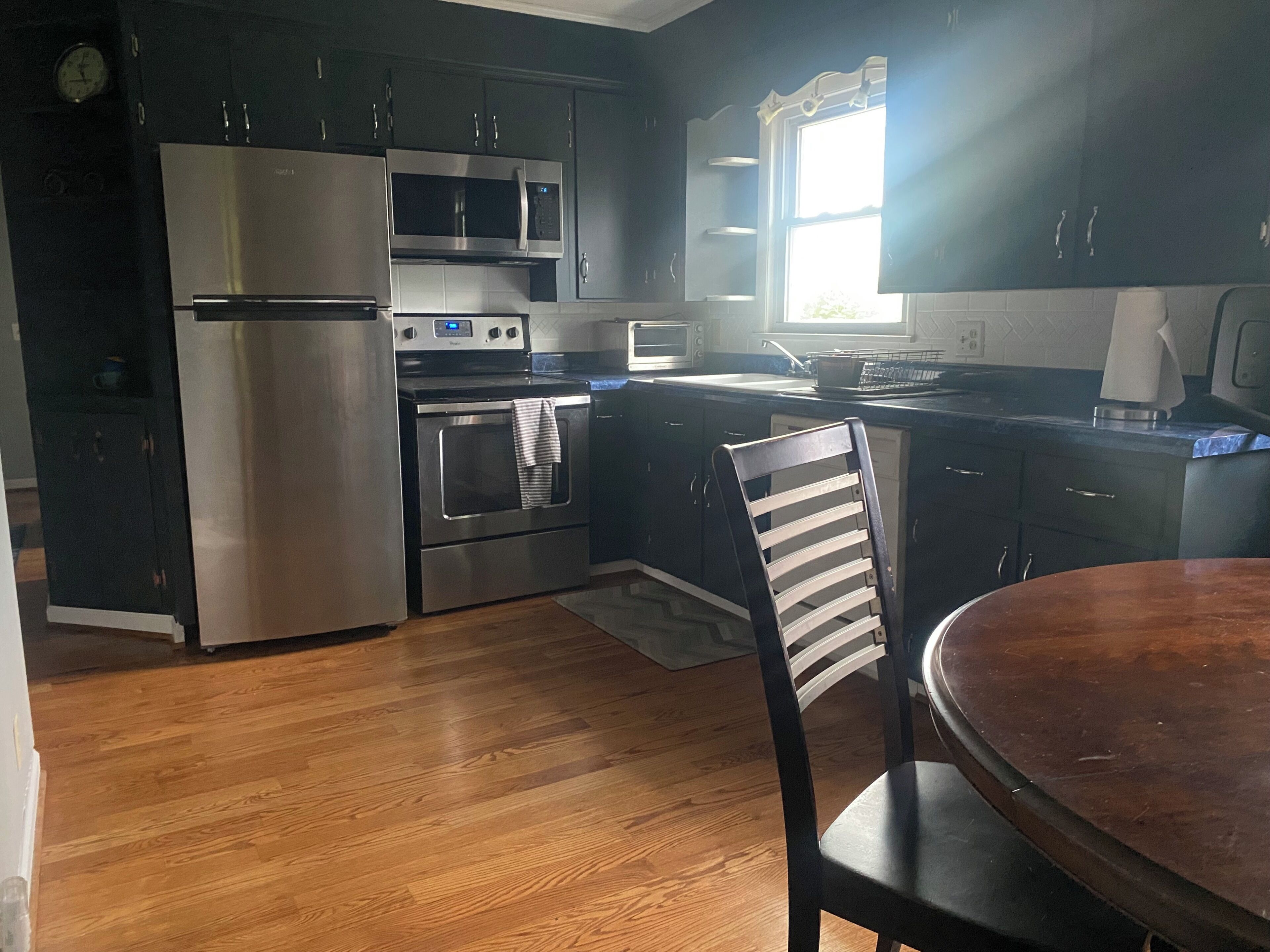 A kitchen with stainless steel appliances, a wooden floor, and a window providing natural light.