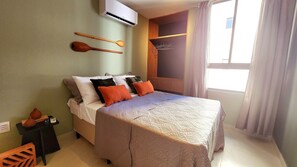 A bedroom with a bed, pillows, a wooden headboard, a wall-mounted air conditioner, a window with curtains, and a small table with a vase and a remote control. - Ancla del Sol by Hosppedar (Cabedelo)