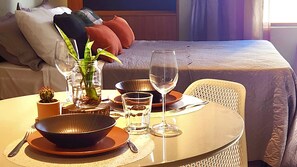 A neatly arranged dining table with a bowl, plates, cutlery, and glasses, set against a bed with pillows and a plant. - Ancla del Sol by Hosppedar (Cabedelo)