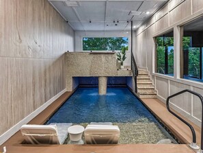 En indendørs swimmingpool med en stenvæg, et lille opholdsområde og en trappe, der fører til en etage over.