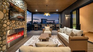 A modern outdoor living space with a stone wall, a fireplace, wicker furniture, and a view of the sky. - The Grotto • Indoor Pool • Rooftop • Sleeps 16 (Sevierville)