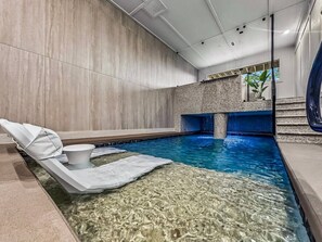 Ein Innenpool mit Liegestuhl und kleinem Tisch, umgeben von Wänden mit strukturierter Oberfläche.