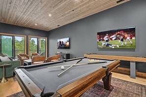 Ein Billardtisch mit Spielzeug und Kugeln, ein Fernseher, der ein Sportspiel zeigt, und eine Sitzecke mit Stühlen und einer Couch.