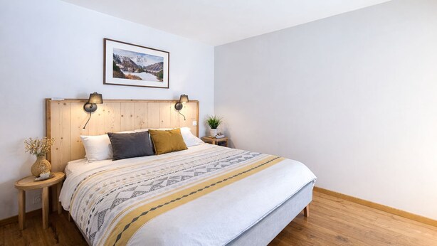 Une chambre à coucher bien rangée, avec une tête de lit en bois, une couvre-lit à motifs et un tableau représentant un paysage, encadré et placé au-dessus du lit.