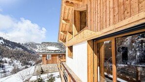 Une cabane en bois avec un toit en pierre, de grandes fenêtres et une vue sur un paysage montagneux enneigé.