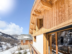 A wooden cabin with a stone roof, large windows, and a view of a snowy mountain landscape.