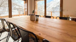 A dining area with a large wooden table and chairs, large windows with a view of a snowy mountain.
