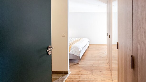 A hallway leading to a bedroom with a bed and a wooden floor.