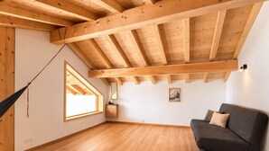 Une pièce avec un plafond en bois incliné, un hamac, un canapé, une petite table et une fenêtre.