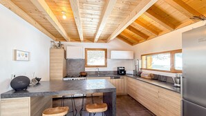 Une cuisine moderne avec des poutres en bois, un îlot central doté de tabourets, un réfrigérateur et une fenêtre laissant entrer la lumière naturelle.