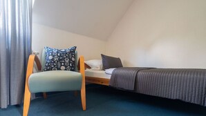 Quarto pequeno com uma cama de solteiro, uma cadeira e mesa de cabeceira.