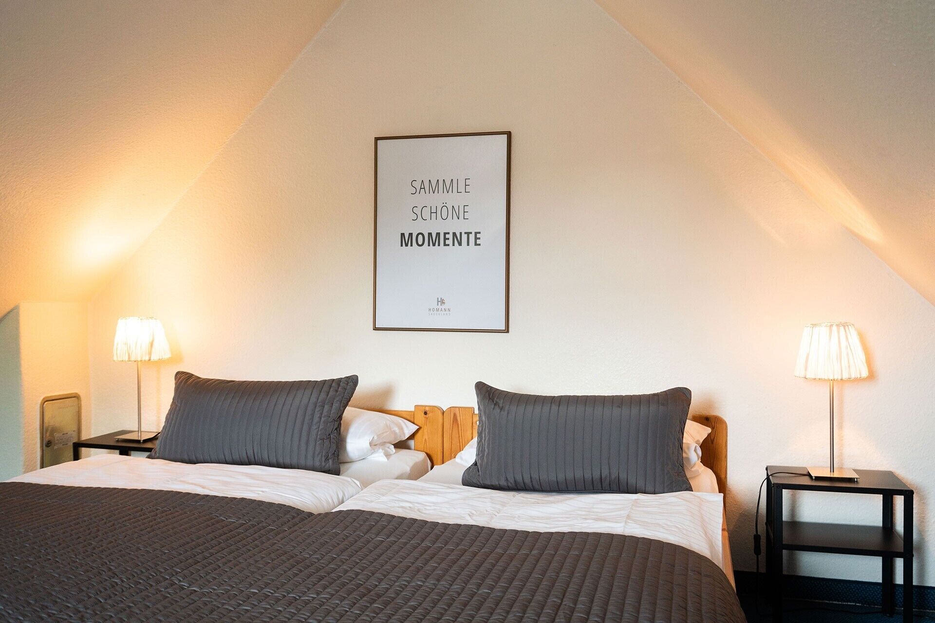 Hotellihuone, jossa on sänky, kaksi yöpöytälamppua, seinällä kehystetty inspiroiva sitaatti ja pieni pöytä, jossa on lamppu.