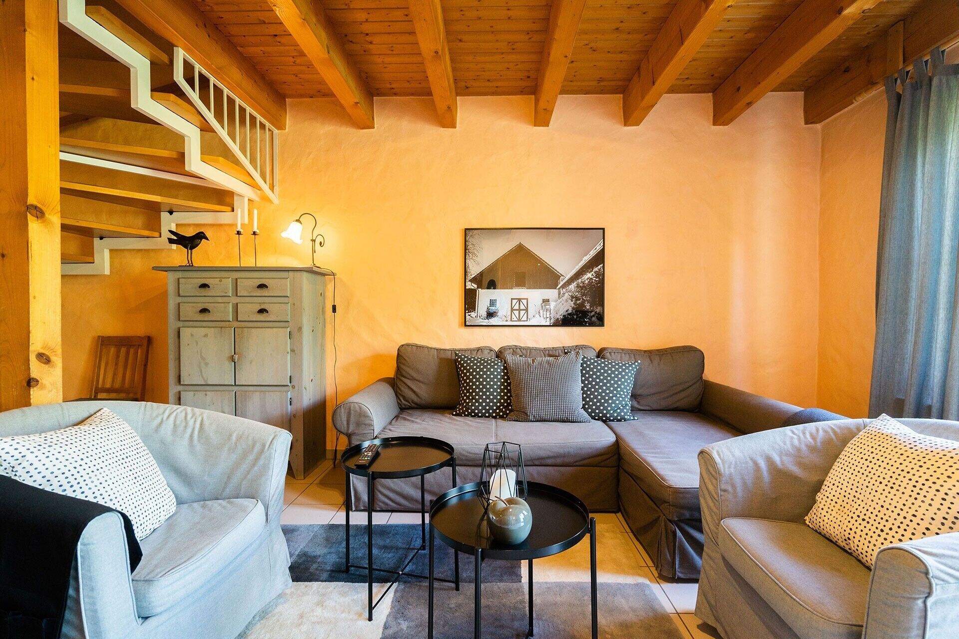 A cozy living room with a sofa, two armchairs, a coffee table, and a staircase.