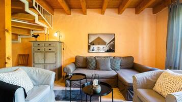 A cozy living room with a sofa, two armchairs, a coffee table, and a staircase.