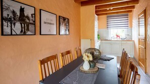 Uma sala de jantar com uma mesa comprida, cadeiras de madeira e quadros nas paredes.