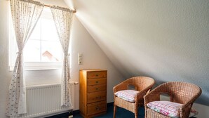 Um quarto com janela, radiador, cómoda de madeira e duas cadeiras de vime.