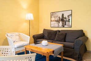Ein Wohnzimmer mit Sofa, Sessel, Lampe, Couchtisch und einem gerahmten Bild an der Wand.